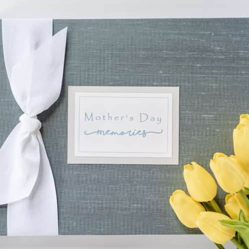 blue silk mother's day memories book with white grosgrain bow and plaque shown with yellow flower props