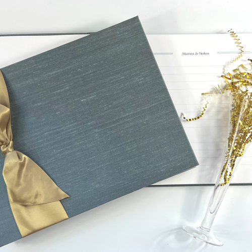 milestone birthday guest book with silver blue silk cover and gold satin ribbon with open page and props