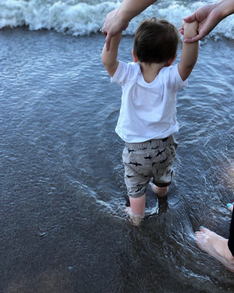 Toddler holding hands with mom walking in the sand